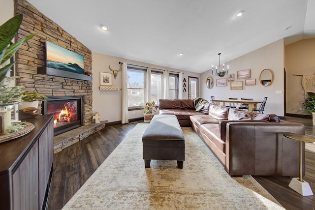 living room with a notable chandelier, a stone fireplace, dark wood-type flooring, and vaulted ceiling