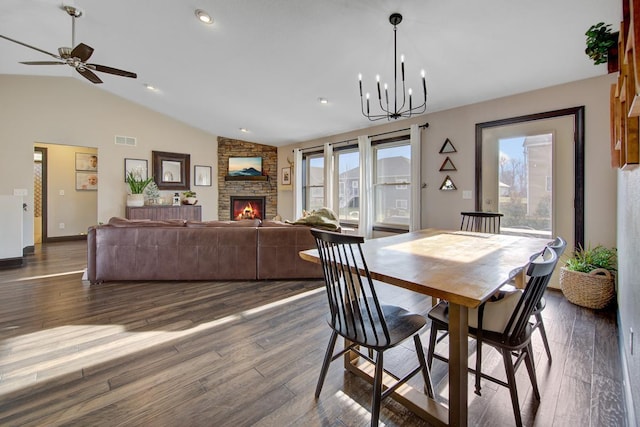 dining area featuring ceiling fan with notable chandelier, dark hardwood / wood-style flooring, a stone fireplace, and lofted ceiling