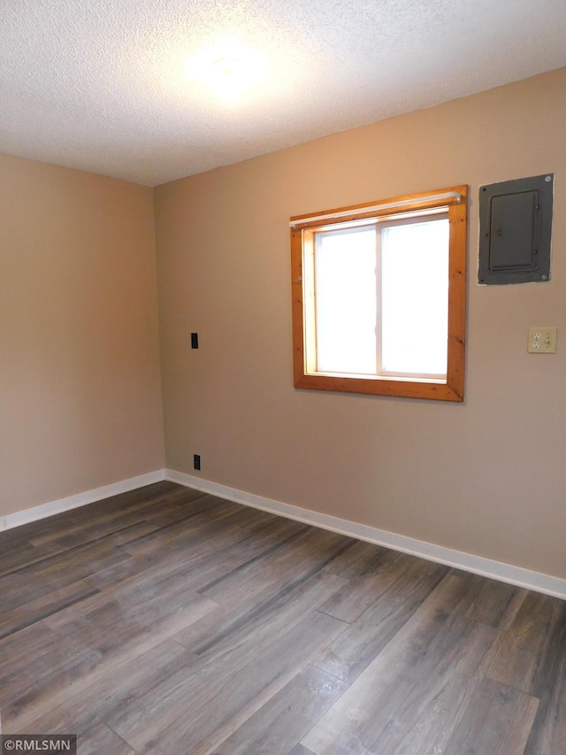 empty room featuring electric panel, dark wood-type flooring, and a textured ceiling