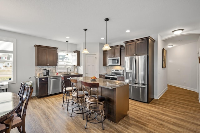 kitchen with dark stone countertops, light wood-type flooring, decorative light fixtures, a kitchen island, and stainless steel appliances