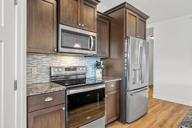 kitchen with appliances with stainless steel finishes, backsplash, dark stone counters, dark brown cabinets, and light hardwood / wood-style flooring