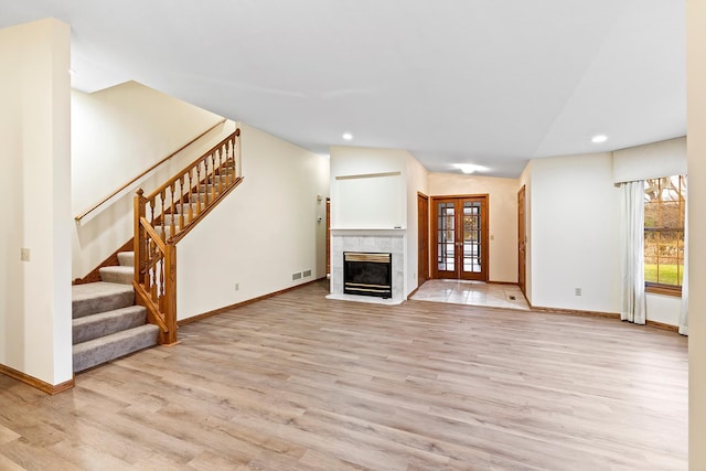 unfurnished living room with a tile fireplace, french doors, lofted ceiling, and light wood-type flooring