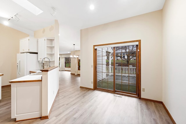 kitchen featuring kitchen peninsula, a skylight, decorative light fixtures, white cabinets, and light hardwood / wood-style floors