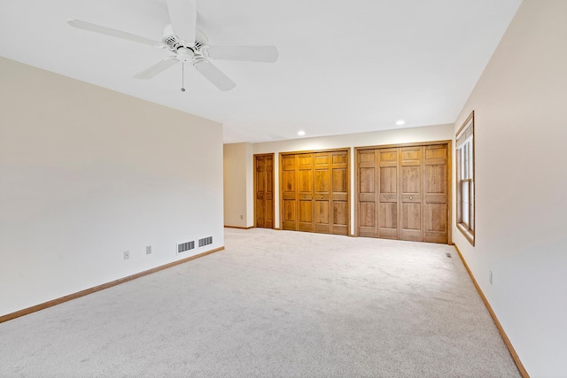 unfurnished bedroom featuring ceiling fan, light carpet, and two closets