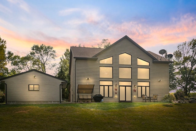 back of house at dusk featuring a shingled roof and a yard