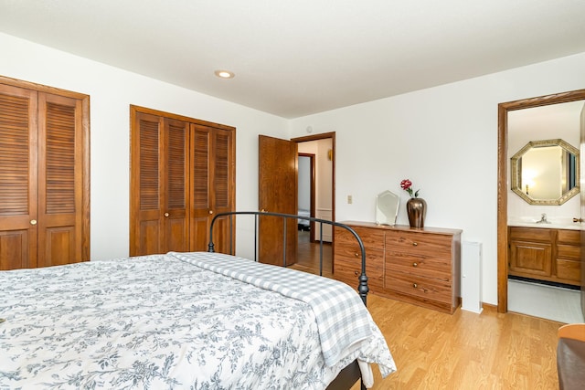 bedroom with light wood finished floors, a sink, two closets, ensuite bath, and recessed lighting