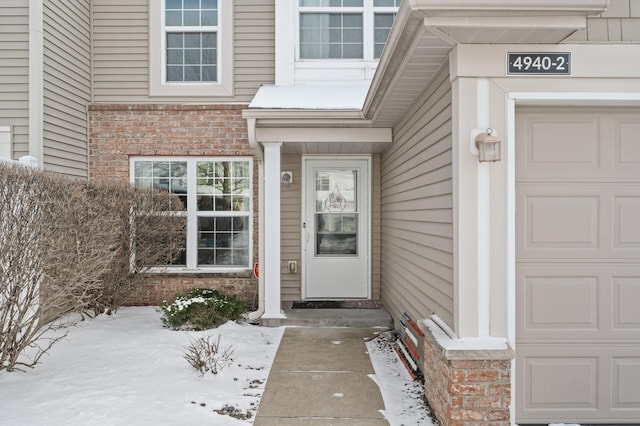 snow covered property entrance featuring a garage