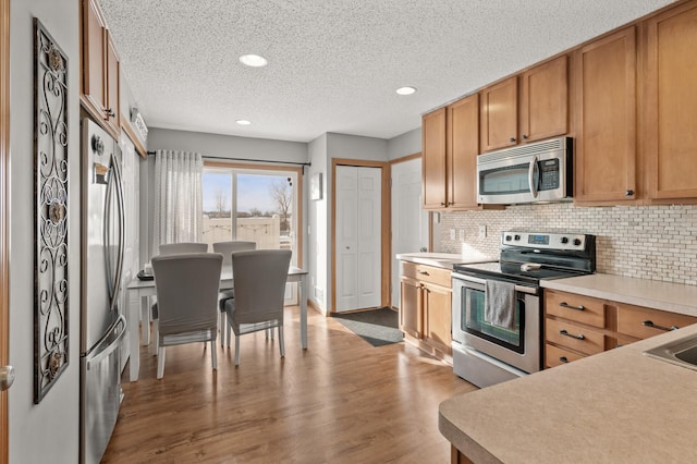 kitchen with light hardwood / wood-style floors, backsplash, stainless steel appliances, and a textured ceiling