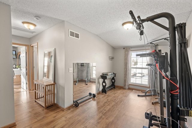 exercise room featuring hardwood / wood-style floors, lofted ceiling, and a textured ceiling