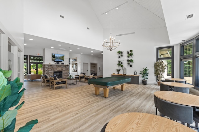 recreation room with billiards, a fireplace, light hardwood / wood-style floors, a towering ceiling, and an inviting chandelier