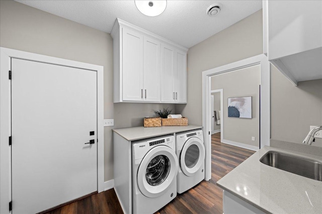 clothes washing area with sink, cabinets, a textured ceiling, dark hardwood / wood-style floors, and washing machine and dryer