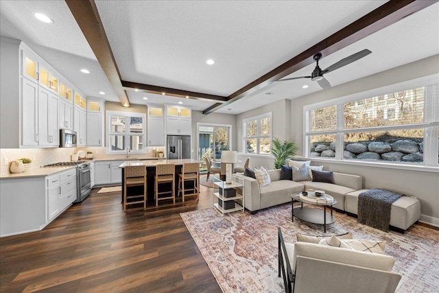 living room featuring dark hardwood / wood-style flooring, ceiling fan, a textured ceiling, and beamed ceiling