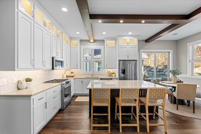 kitchen with beamed ceiling, white cabinetry, sink, a center island, and stainless steel appliances