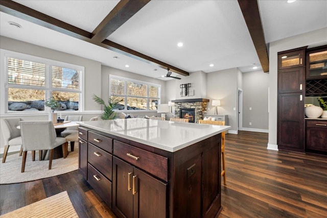 kitchen featuring dark brown cabinetry, dark hardwood / wood-style flooring, a kitchen island, beamed ceiling, and a fireplace