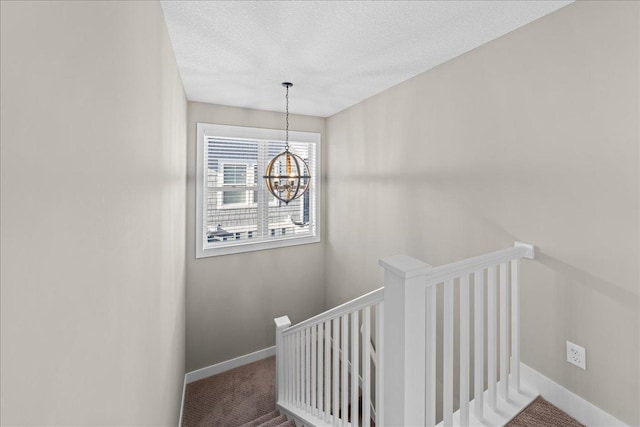 staircase featuring an inviting chandelier, carpet floors, and a textured ceiling