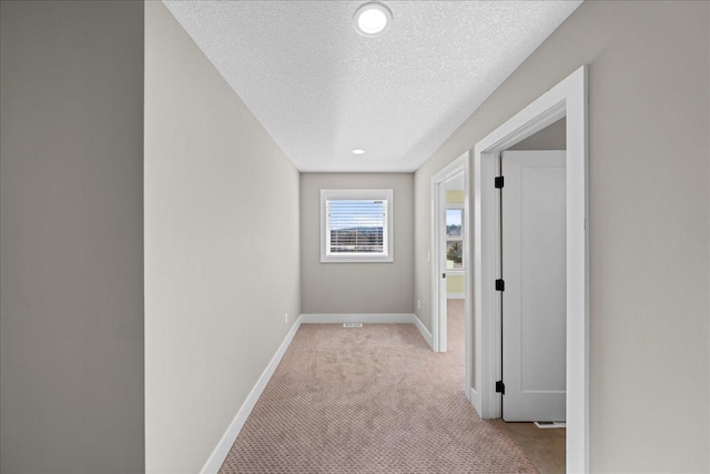 corridor featuring light colored carpet and a textured ceiling