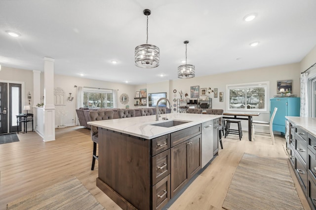 kitchen featuring sink, dark brown cabinets, light hardwood / wood-style flooring, hanging light fixtures, and a center island with sink