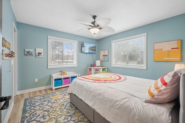 bedroom featuring ceiling fan, a textured ceiling, multiple windows, and light wood-type flooring