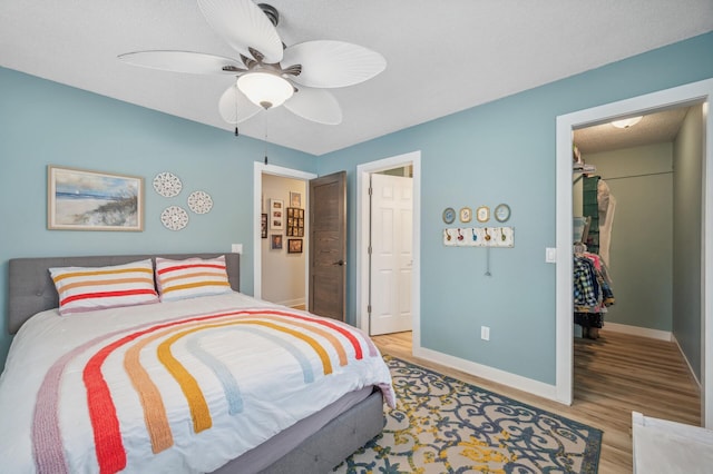 bedroom with a walk in closet, a textured ceiling, light wood-type flooring, a closet, and ceiling fan