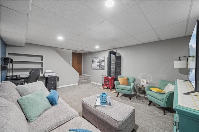 carpeted living room with built in shelves, a paneled ceiling, and a wood stove