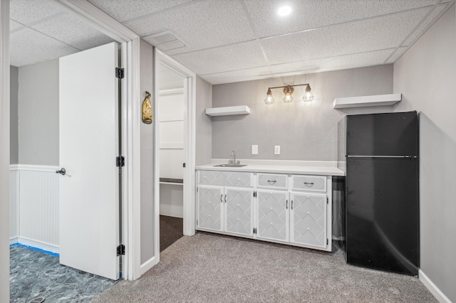 kitchen with a drop ceiling, sink, carpet floors, and black fridge