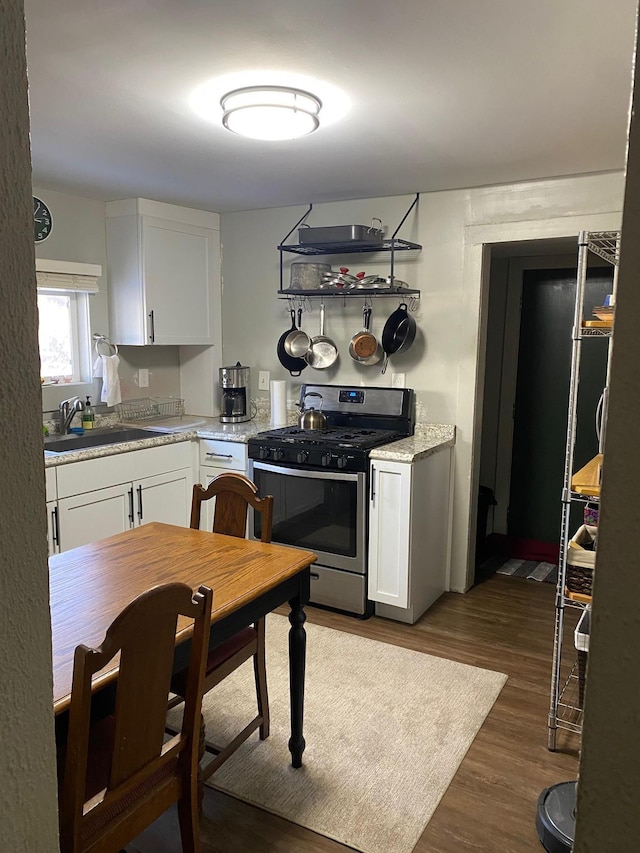 kitchen featuring stainless steel gas range oven, sink, dark hardwood / wood-style floors, light stone countertops, and white cabinetry