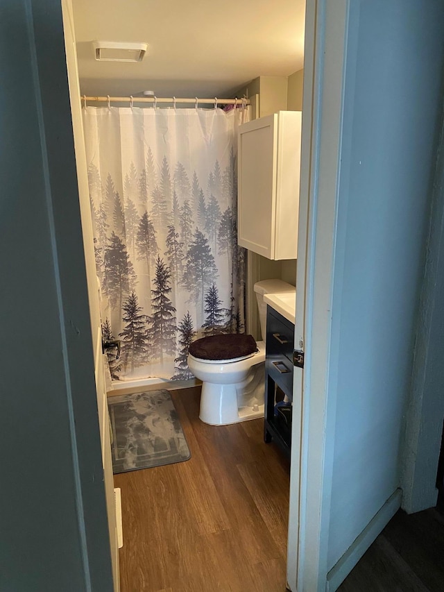 bathroom with hardwood / wood-style floors, toilet, and a shower with curtain