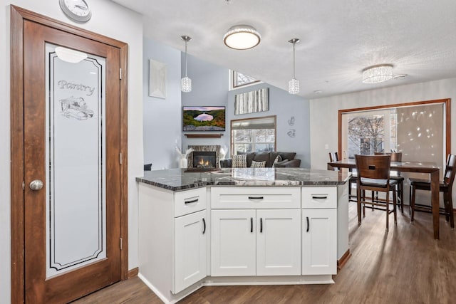 kitchen with a fireplace, dark hardwood / wood-style flooring, decorative light fixtures, and white cabinetry