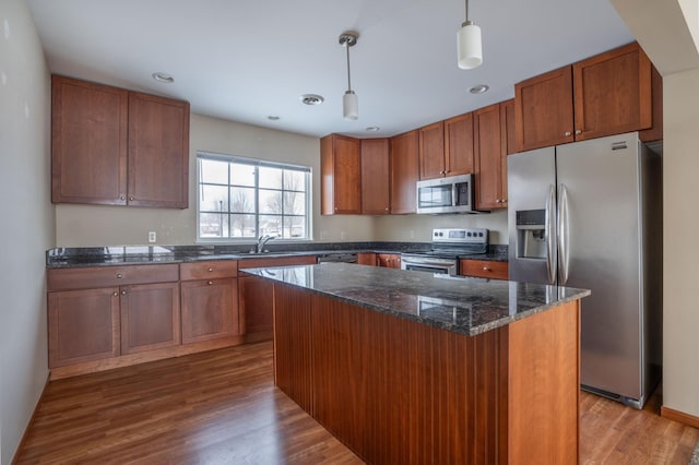 kitchen with appliances with stainless steel finishes, wood-type flooring, sink, hanging light fixtures, and a center island