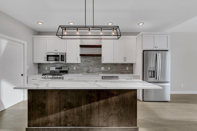 kitchen featuring light stone counters, stainless steel appliances, sink, pendant lighting, and white cabinets