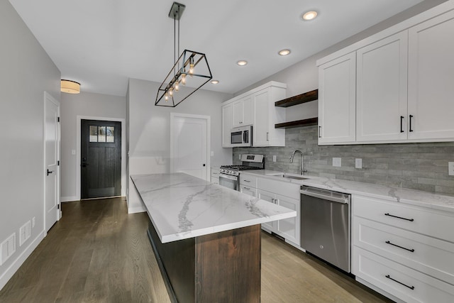 kitchen featuring appliances with stainless steel finishes, sink, decorative light fixtures, a center island, and white cabinetry