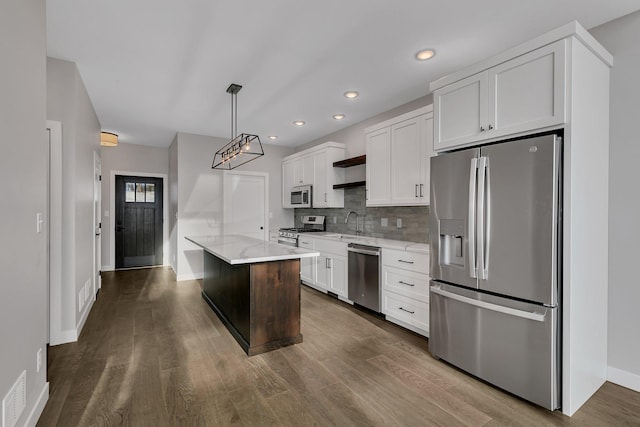 kitchen with decorative light fixtures, a kitchen island, white cabinetry, and appliances with stainless steel finishes