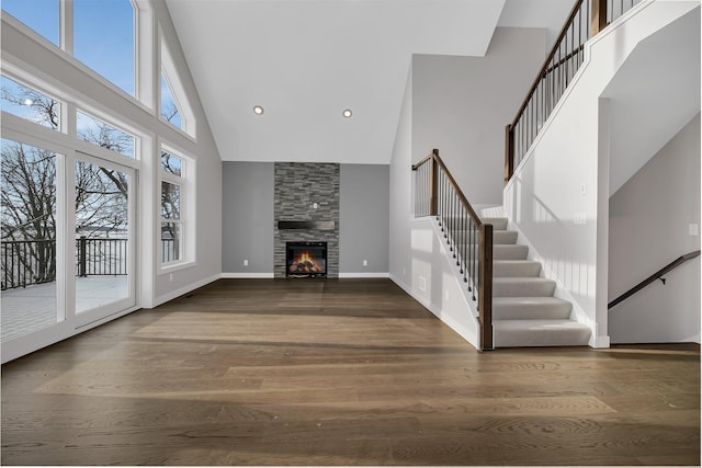 unfurnished living room featuring dark hardwood / wood-style flooring, a towering ceiling, and a stone fireplace