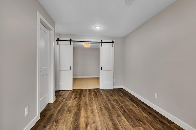 unfurnished bedroom featuring dark hardwood / wood-style floors and a barn door