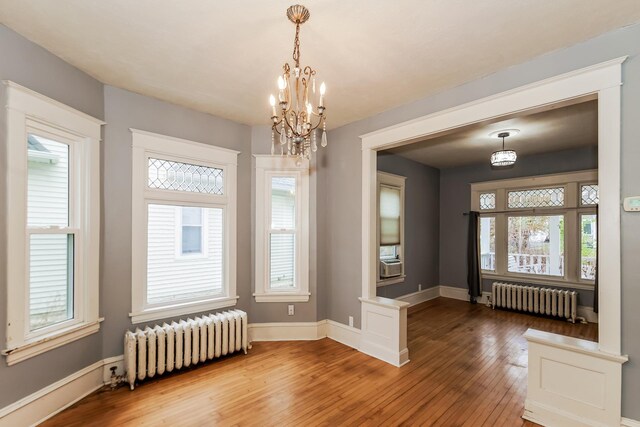 unfurnished dining area featuring hardwood / wood-style floors, radiator heating unit, and an inviting chandelier