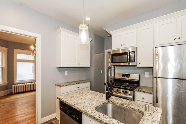 kitchen featuring radiator heating unit, appliances with stainless steel finishes, pendant lighting, white cabinets, and hardwood / wood-style flooring