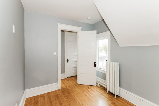 unfurnished bedroom with a closet, light hardwood / wood-style floors, vaulted ceiling, and radiator