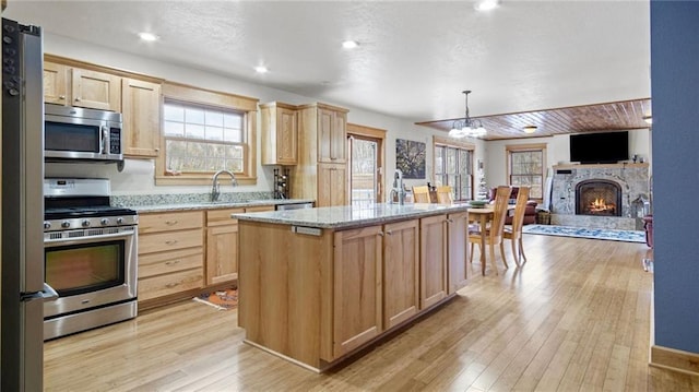 kitchen featuring stainless steel appliances, light stone counters, light hardwood / wood-style floors, light brown cabinetry, and a kitchen island