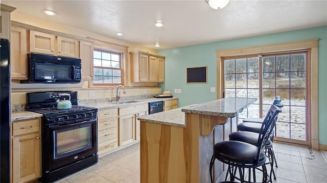 kitchen featuring light stone countertops, a kitchen bar, sink, black appliances, and a kitchen island