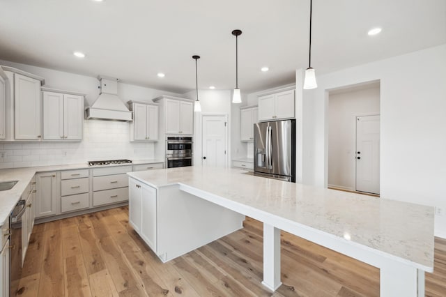 kitchen featuring decorative light fixtures, appliances with stainless steel finishes, a center island, and custom range hood