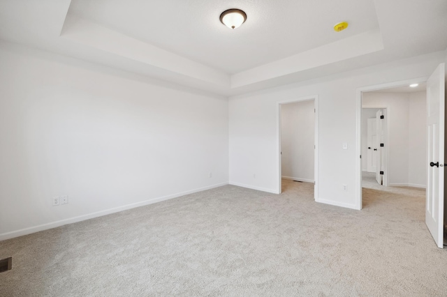 unfurnished bedroom with light colored carpet and a tray ceiling