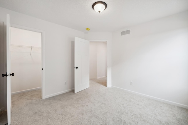 unfurnished bedroom featuring a spacious closet, light colored carpet, and a closet