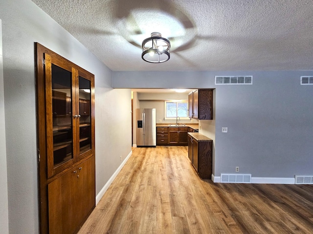 corridor featuring a textured ceiling, light wood-type flooring, and sink