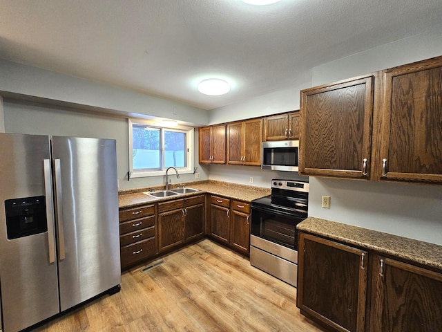 kitchen featuring a textured ceiling, stainless steel appliances, light hardwood / wood-style floors, and sink