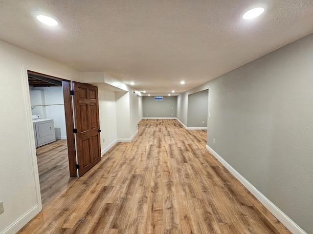 hallway with light hardwood / wood-style floors, a textured ceiling, and washer / clothes dryer