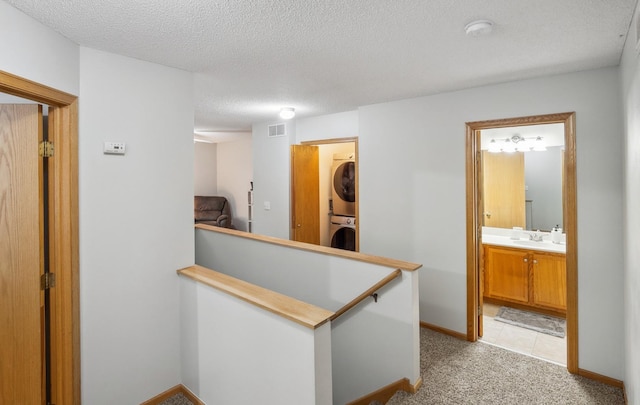 hall featuring light carpet, a textured ceiling, stacked washer / drying machine, and sink