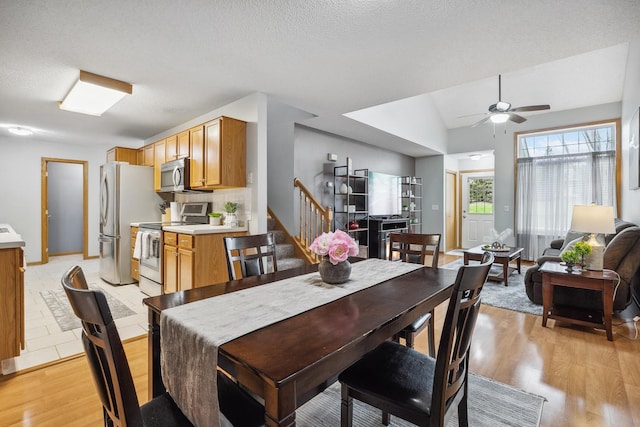 dining space with a textured ceiling, ceiling fan, vaulted ceiling, and light wood-type flooring