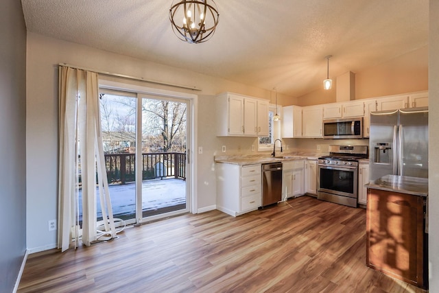 kitchen with lofted ceiling, white cabinets, sink, appliances with stainless steel finishes, and decorative light fixtures