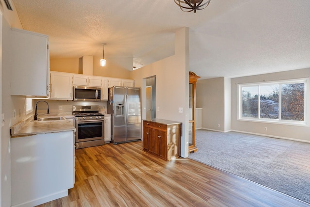 kitchen with stainless steel appliances, vaulted ceiling, decorative light fixtures, light hardwood / wood-style flooring, and white cabinetry