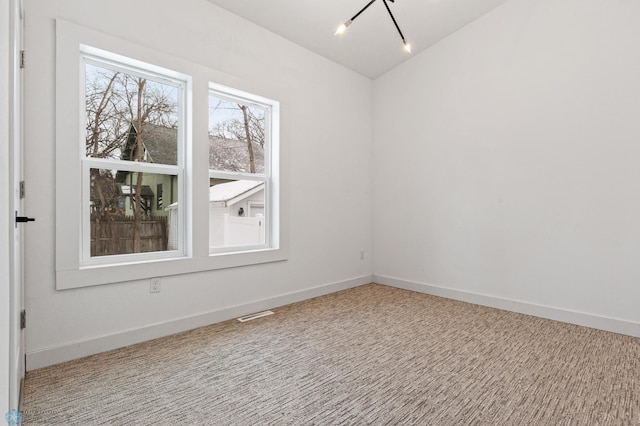 carpeted empty room with an inviting chandelier and lofted ceiling